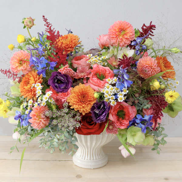 Colorful mixed bouquet in a white vase with dahlias, roses, and blue flowers
