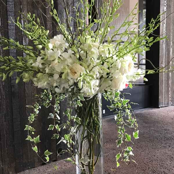 Tall white floral arrangement in a clear glass vase with trailing ivy