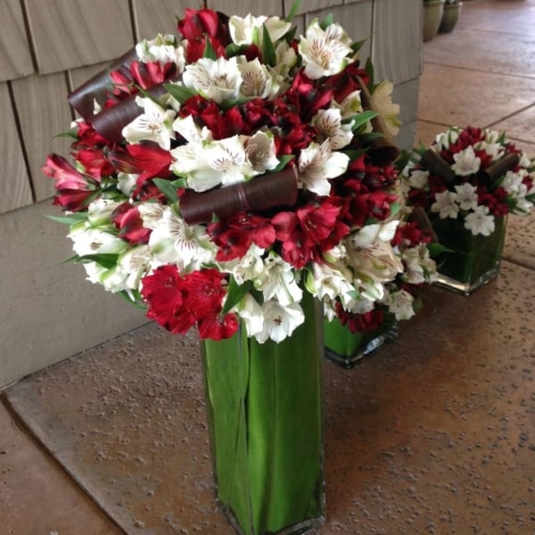 Red and white flower arrangement in a tall green vase with dark ribbon accents