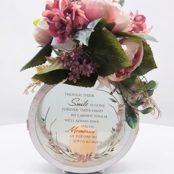 Pink floral arrangement on a memorial plaque with a candle graphic