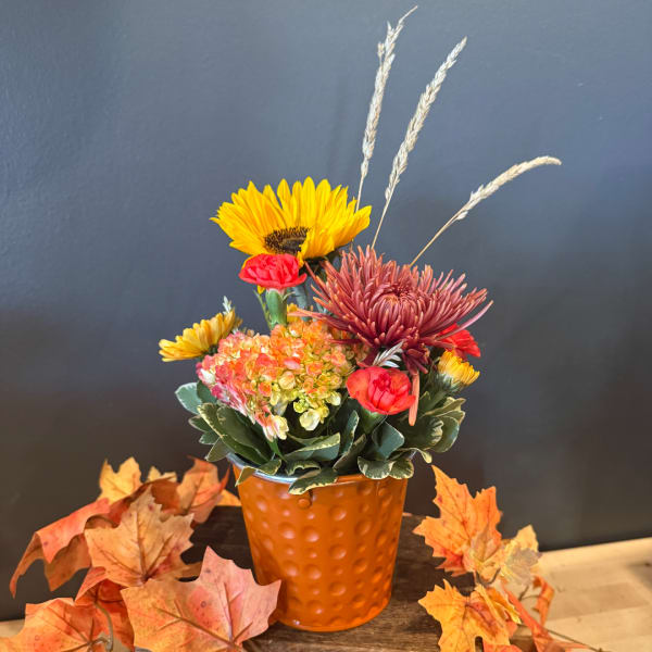 Fall floral arrangement in an orange textured vase with sunflowers and chrysanthemums
