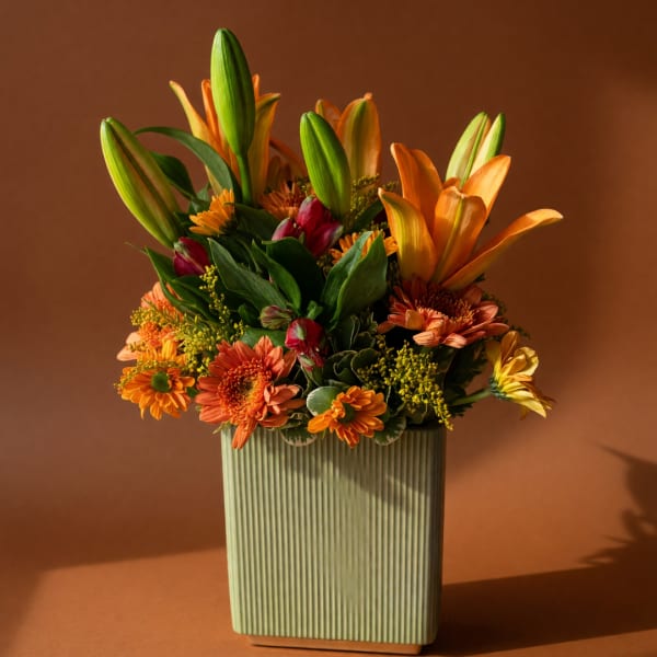 Orange lilies and mixed orange flowers in a ribbed rectangular vase