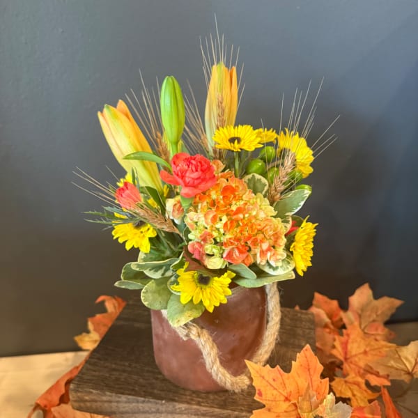 Autumn floral arrangement in a rope-wrapped vase with yellow blooms and orange lilies