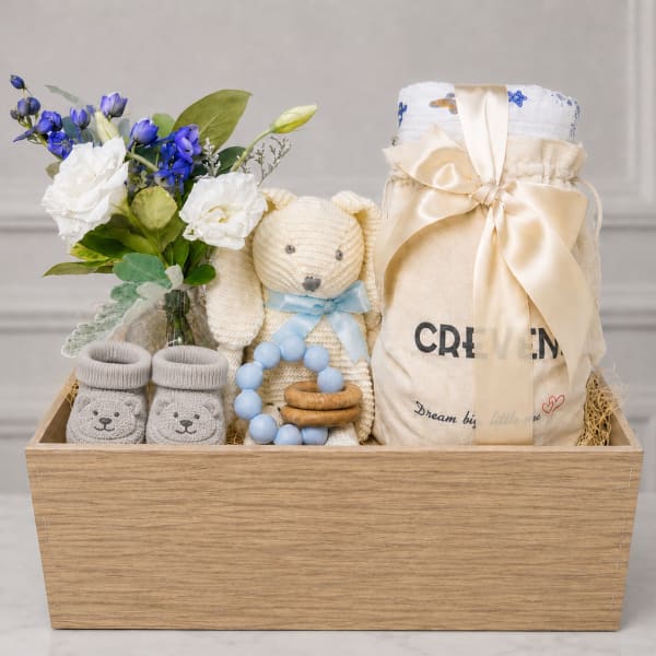Gift basket with white and blue flowers, baby socks, a teddy bear, and baby items