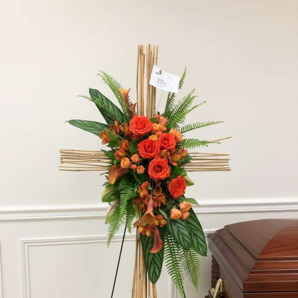 Orange rose funeral spray on a bamboo cross stand beside a casket