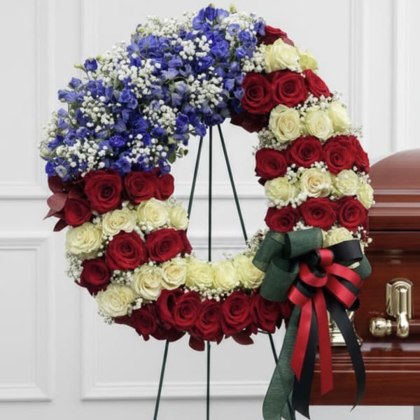 Circular wreath of red and cream roses with blue flowers on a stand