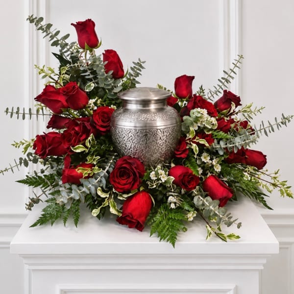 Red roses arranged around a silver urn on a white pedestal
