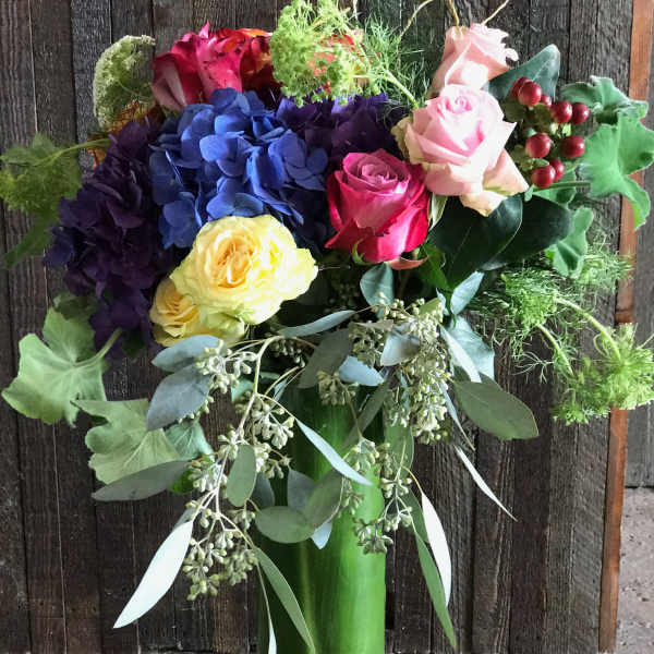 Colorful bouquet of roses and hydrangeas in a tall glass vase