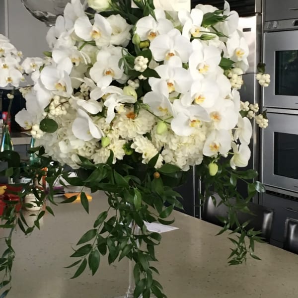 Large white orchid arrangement in a clear vase with trailing greenery