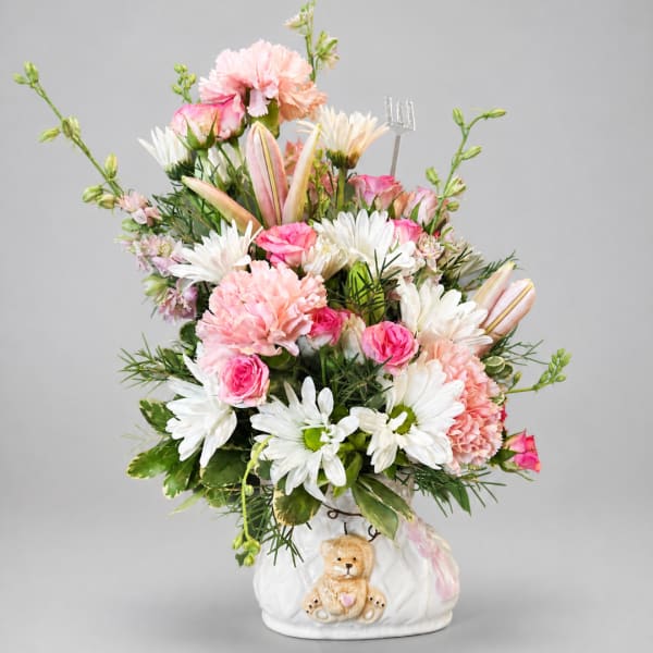 Pink and white mixed bouquet in a white ceramic vase with a teddy bear decoration.
