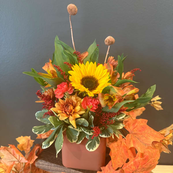Autumn floral arrangement with a sunflower and orange blooms in a pink vase
