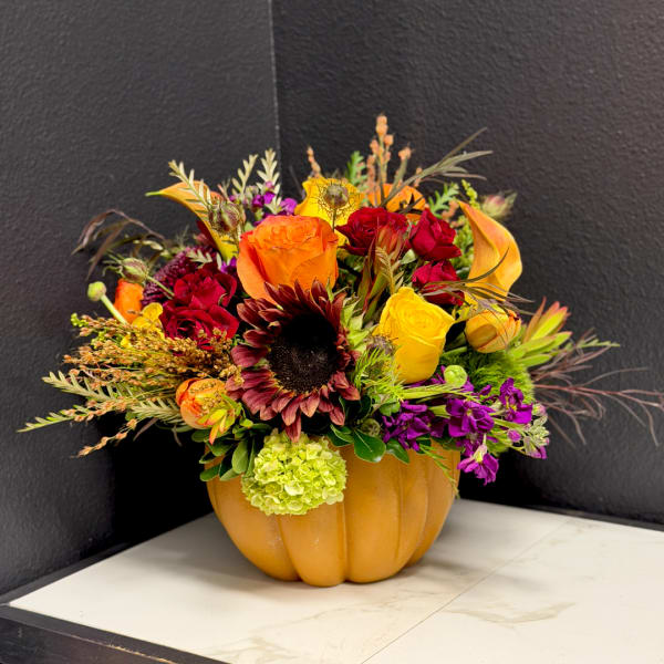 Mixed bouquet in a pumpkin-shaped vase with orange, red, yellow, and purple flowers