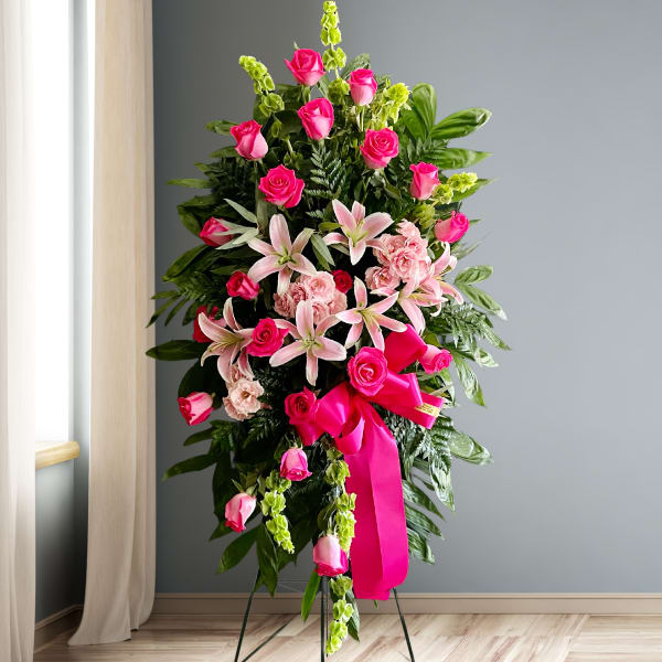 Tall standing floral spray with pink roses and lilies on a ribboned easel