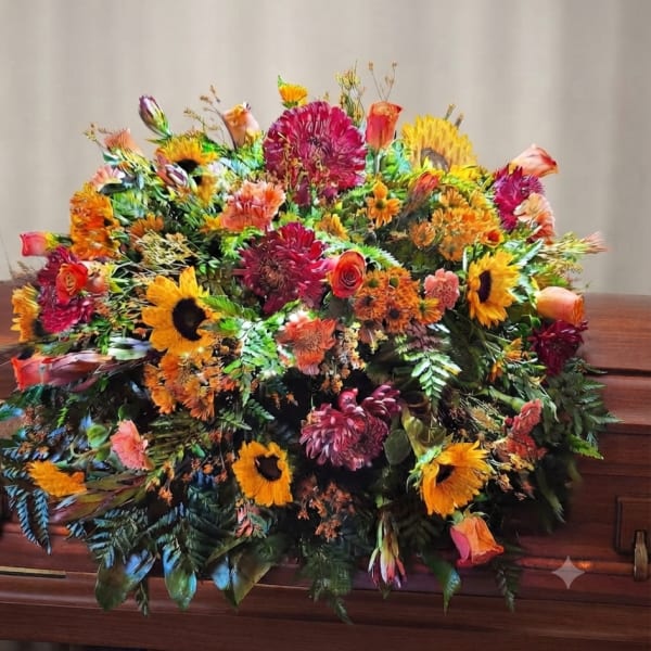 Large colorful floral casket spray with sunflowers, roses, and mums