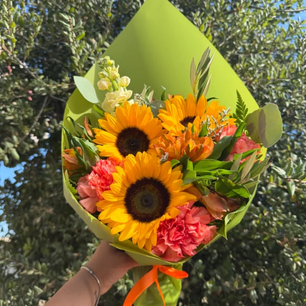 Bouquet of sunflowers and pink carnations wrapped in green paper