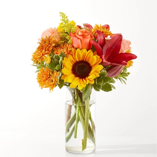 Mixed bouquet with sunflowers, roses, and lilies in a clear glass vase