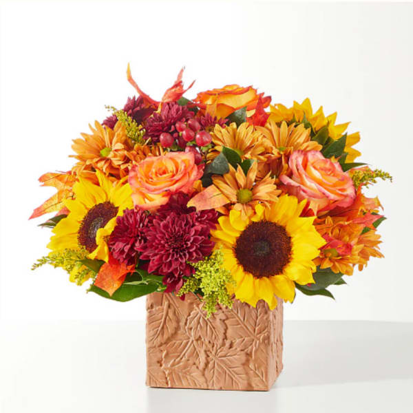 Autumn bouquet of sunflowers, roses, and mums in a leaf-patterned vase