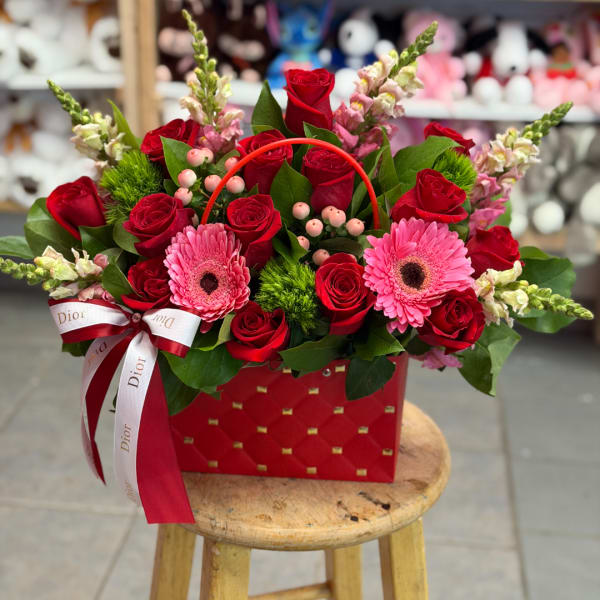 Red roses and pink gerbera daisies in a red gift bag with ribbon