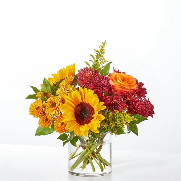 Colorful bouquet of sunflowers, chrysanthemums, and a rose in a glass vase