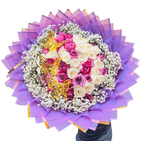 Round bouquet of pink and white roses with purple wrapping and butterfly picks