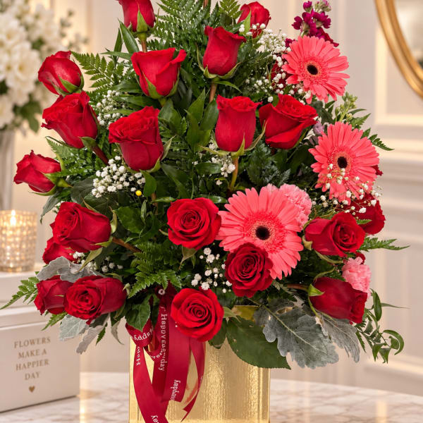 Red roses and pink gerbera daisies arranged in a gold vase
