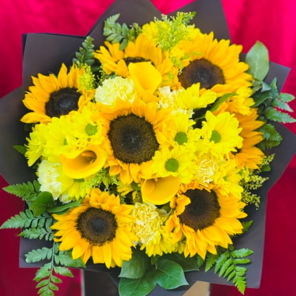Bouquet of sunflowers, yellow calla lilies, and white blooms in black wrap