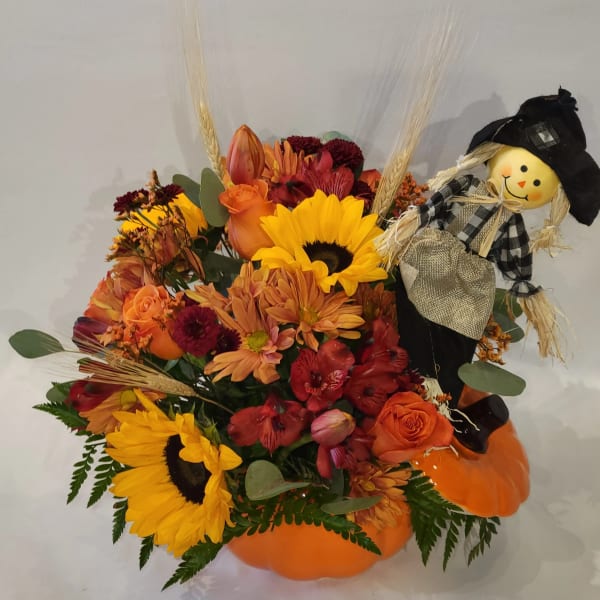Autumn floral arrangement in a pumpkin container with a scarecrow decoration