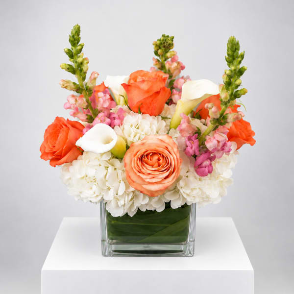 Orange and white floral arrangement in a square glass vase