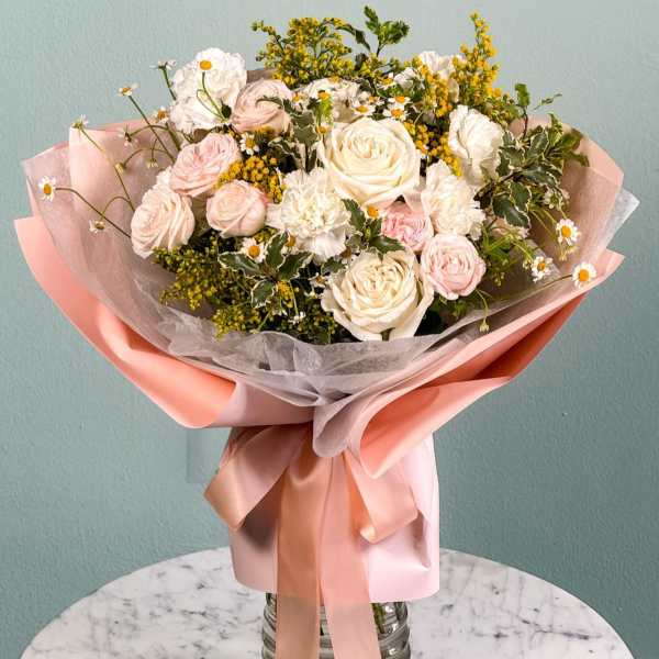 Bouquet of pale pink and white roses with small daisies wrapped in pink paper
