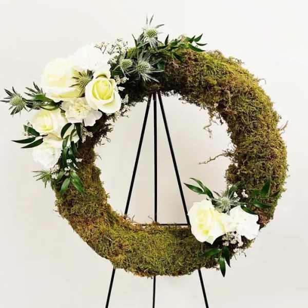 Moss wreath with white roses and thistle on a black stand