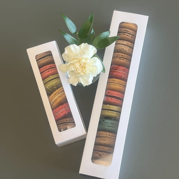 White carnation with green leaves beside two macaron gift boxes