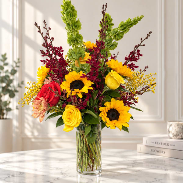 Mixed bouquet with sunflowers, roses, and orchids in a clear glass vase