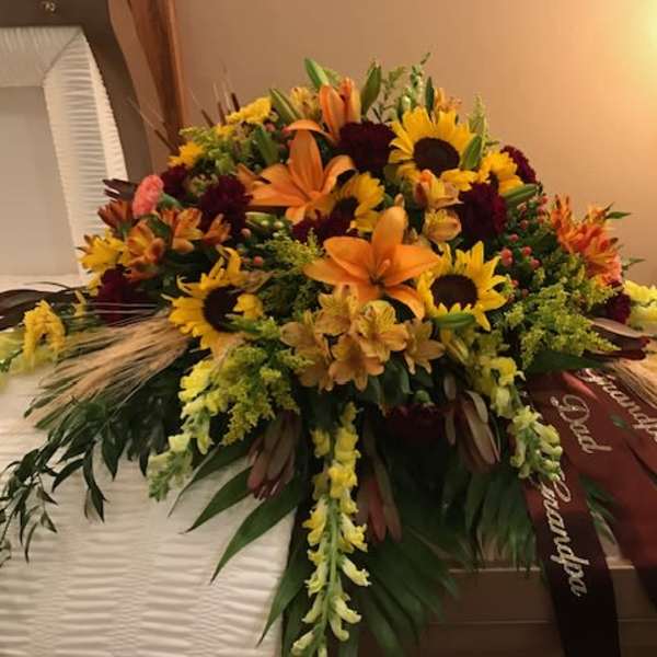Large floral casket spray with sunflowers, lilies, and orange blooms