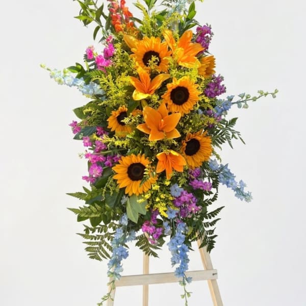 Tall floral spray with sunflowers, lilies, and blue and purple accents on an easel