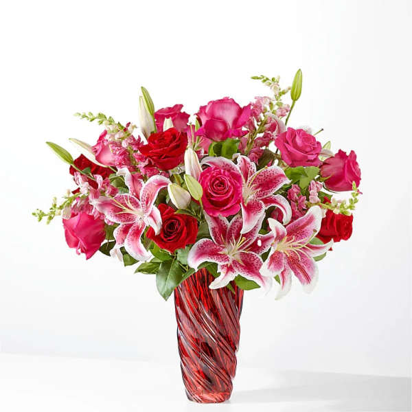 Pink and red roses with lilies in a red glass vase