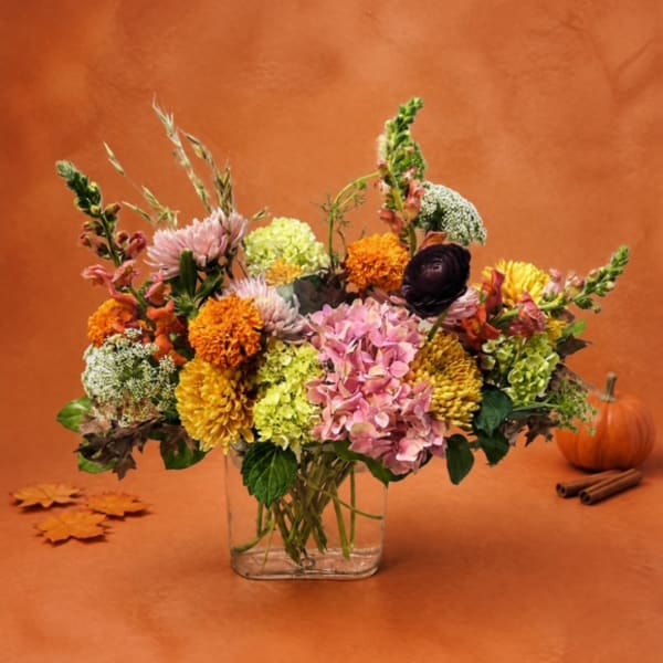 Mixed fall bouquet in a clear glass vase with pink, orange, yellow, and green blooms
