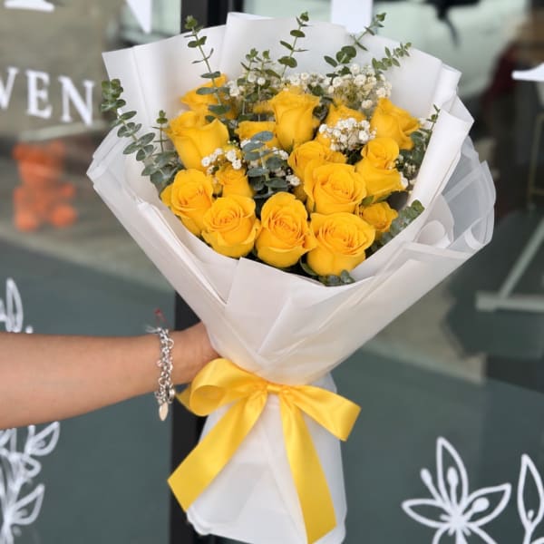 Bouquet of yellow roses wrapped in white paper with a yellow ribbon