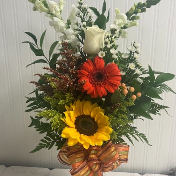 Tall mixed bouquet with sunflowers, a red gerbera daisy, and white blooms in a glass vase
