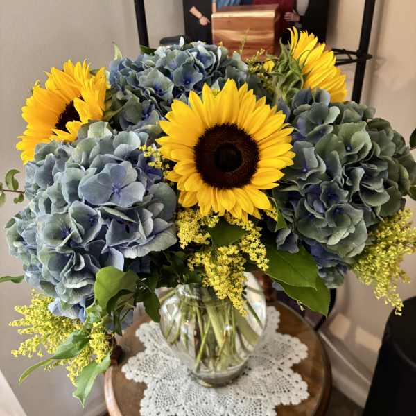 Bouquet of sunflowers and blue hydrangeas in a clear glass vase