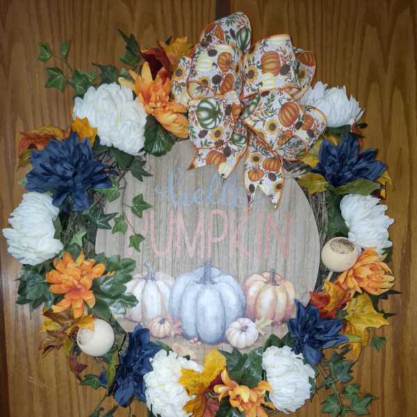 Fall wreath with white and orange flowers, blue accents, and a pumpkin ribbon