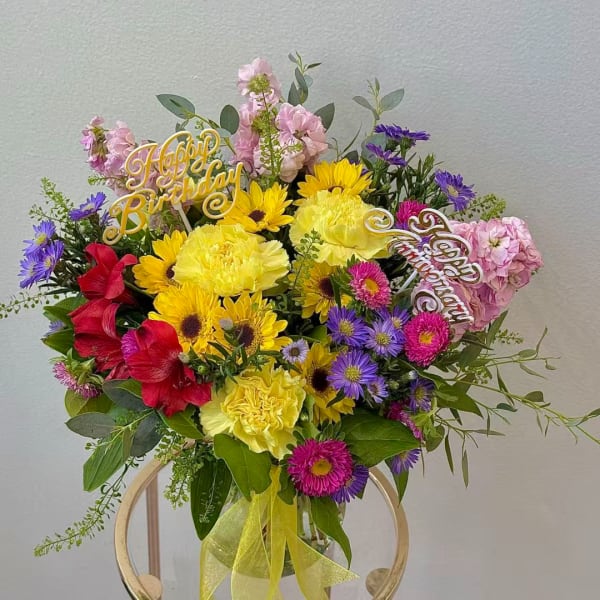 Colorful birthday bouquet with yellow, pink, purple, and red flowers in a glass vase