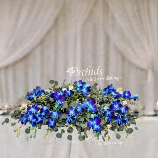 Low floral arrangement with vivid blue orchids and greenery on a wedding table