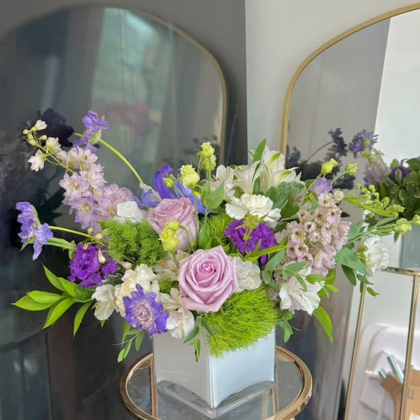 Lavender and white floral arrangement in a square glass vase