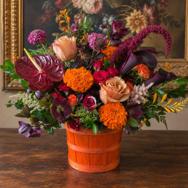 Mixed floral arrangement in an orange wooden basket with burgundy and peach blooms