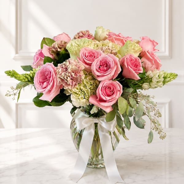 Pink roses and carnations in a glass vase with a white ribbon