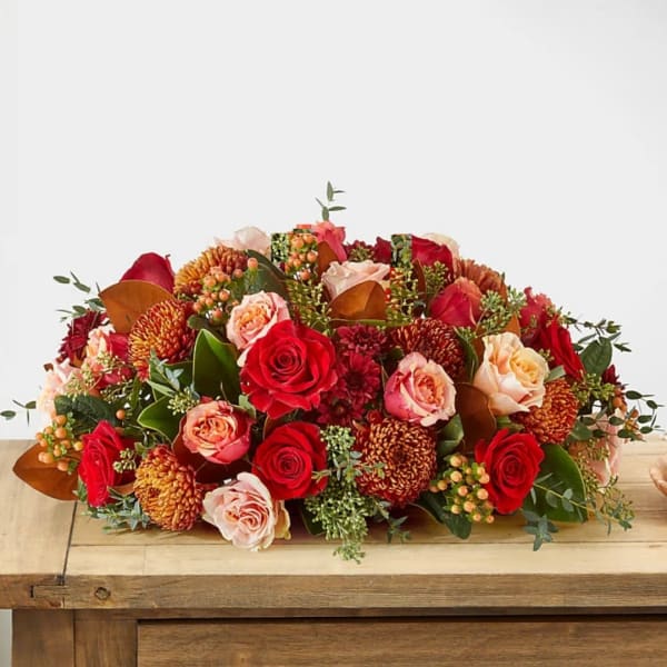 Low arrangement of red and peach roses with orange mums on a wooden table