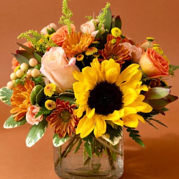 Bouquet of sunflowers, roses, and mums in a clear glass vase