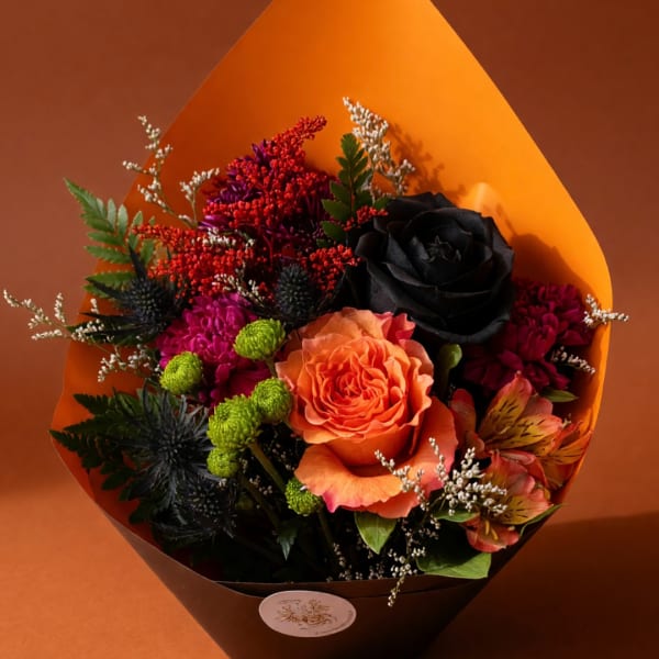 Bouquet with orange and black roses, magenta blooms, and orange wrap