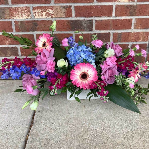 Colorful mixed flower arrangement with pink gerberas and roses in a white container