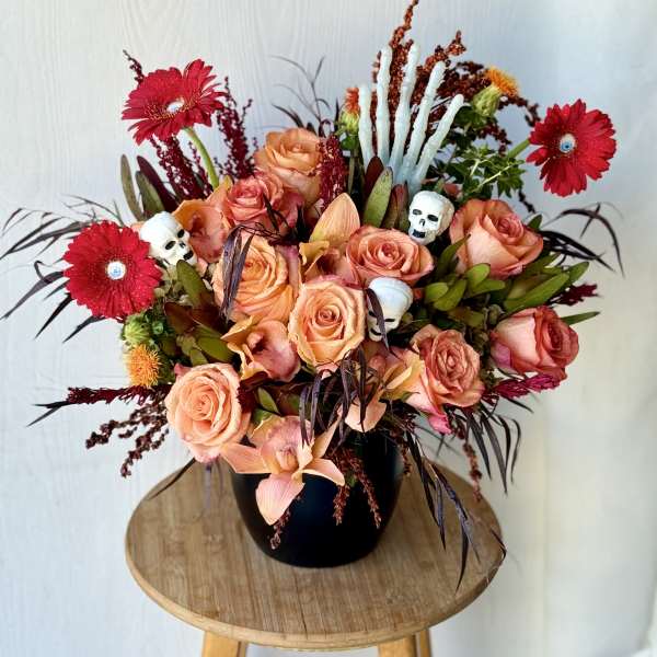 Peach roses and red gerbera daisies in a black vase with skull accents